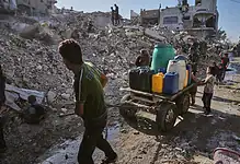 Palestinians collect and transport water through the rubble-strewn streets of Gaza City following heavy destruction.