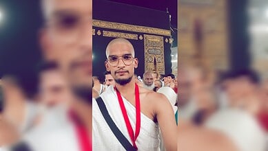 Abdul Shoeb Mohammed standing in front of the Kaaba during Umrah, wearing ihram and glasses, with pilgrims in the background.