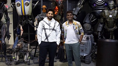 Two young men standing with advanced robots and sci-fi props at a technology expo.