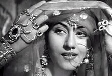 Woman in traditional Indian bridal attire with jewelry and veil, smiling softly.