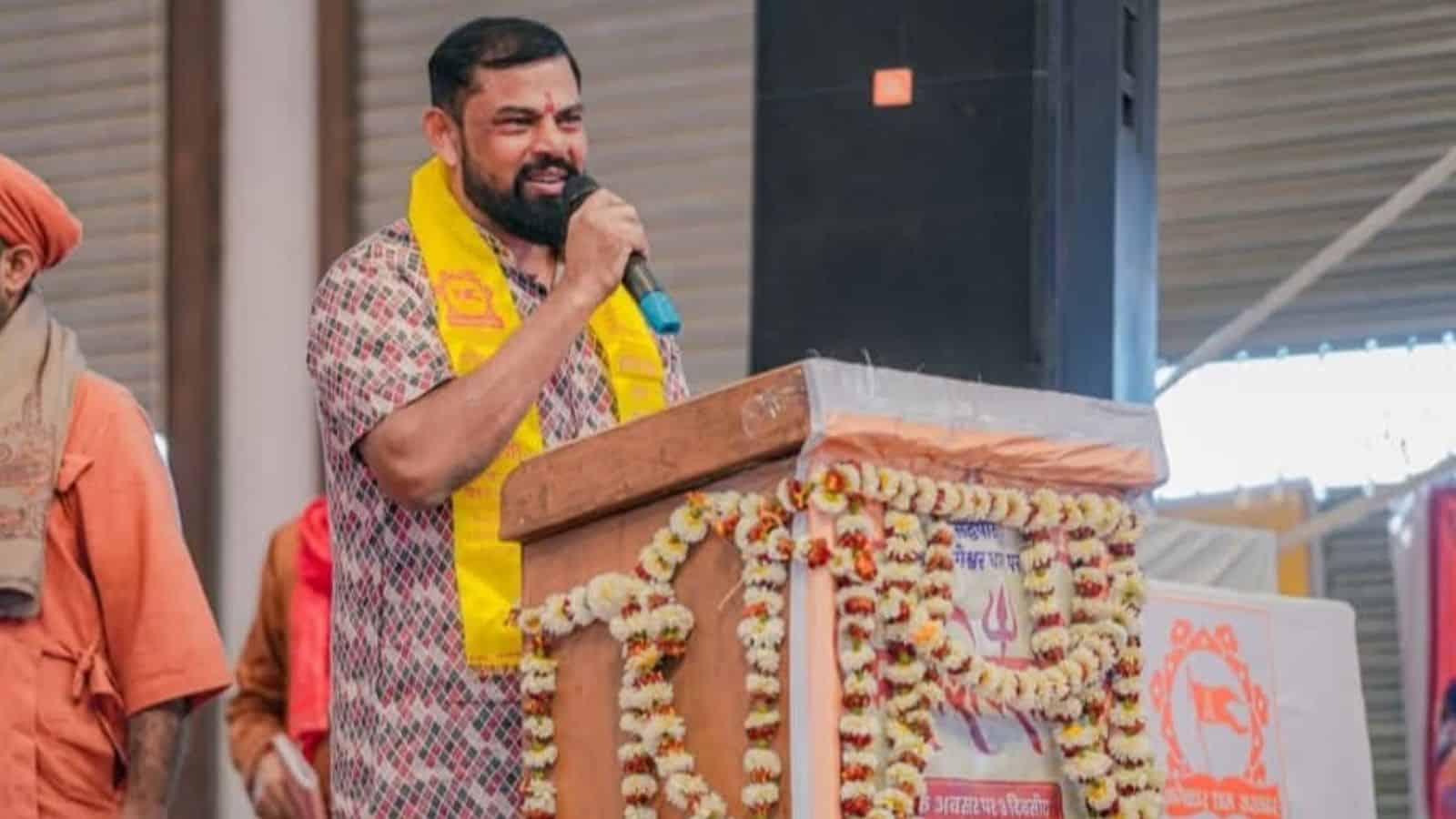 Raja Singh speaking at a rally with a microphone, wearing a yellow scarf, during a political gatheri.