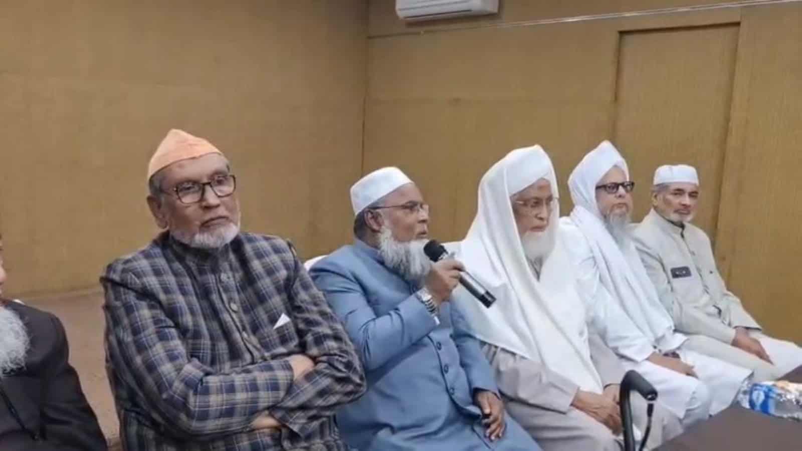 Prominent Muslim leaders participating in a discussion at a formal event in a conference room.