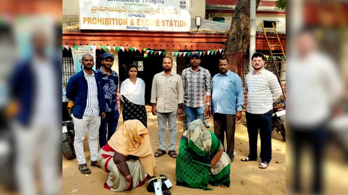 Image shows Two women crouching with heads covered in front of officers at the Nampally Prohibition & Excise Station, Telangana.