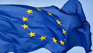 EU flag with yellow stars on a blue background, symbolising unity and cooperation.