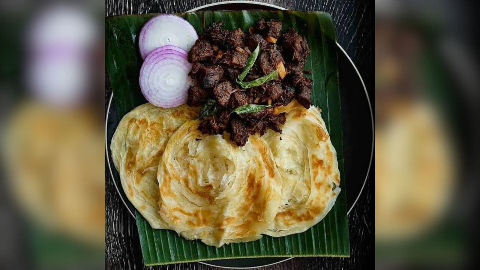 Delicious spicy beef served with crispy paratha and fresh onion slices on a banana leaf. Traditional Indi.