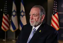 US Ambassador to Israel Mike Huckabee speaks during an interview, with Israeli and US flags in the background.
