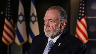 US Ambassador to Israel Mike Huckabee speaks during an interview, with Israeli and US flags in the background.