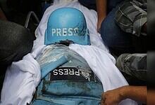 Protester wearing a blue helmet and press badge during a demonstration, surrounded by people.