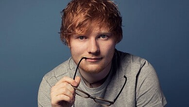 Ed Sheeran with glasses, reflecting on a difficult day, in a close-up portrait.