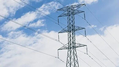 Power transmission tower with high-voltage lines against a blue sky with clouds.