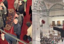 Woman throws headscarf from upper level during protest at Istanbul’s Fatih Mosque as men look on below.