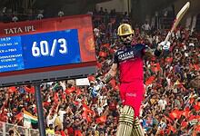 Cricket player in pink uniform hits a six during IPL match, with cheering crowd and scoreboard in backgro.