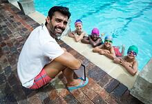 Male swimming coach with four children in goggles at the poolside during summer sports coaching camp.
