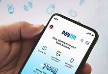 Close-up of a hand holding a smartphone displaying the Paytm app with banking options.