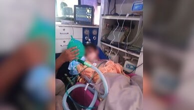 Boy in hospital bed with medical equipment and monitors, receiving oxygen therapy after balcony fall inci.