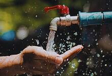 Close-up of a hand catching water from a leaking outdoor tap with blurred greenery background.