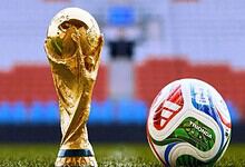 Golden FIFA World Cup trophy and a colourful football on a stadium pitch.