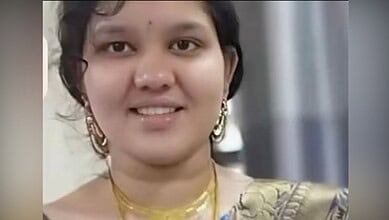 A woman smiling, wearing traditional Indian attire and jewelry, indoors.