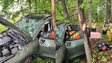 Car accident in wooded area with emergency responders on site.