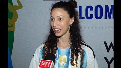 An image of Indian cricketer Smriti Mandhana speaking at a public event, wearing a sports jersey with a s.