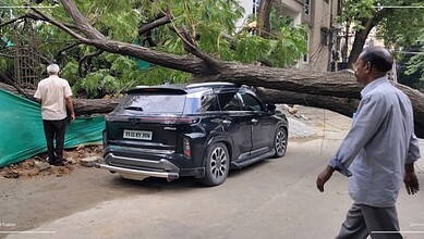 Tree fallen on car in Kukatpally after storm, causing damage and blocking the road.