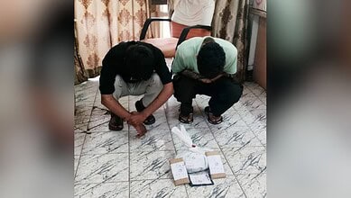 Two men bowing in prayer on a marble floor with a Quran and prayer beads in front of them.
