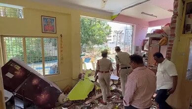 Interior of a house damaged by an explosion, with debris and police officers inspecting the scene.