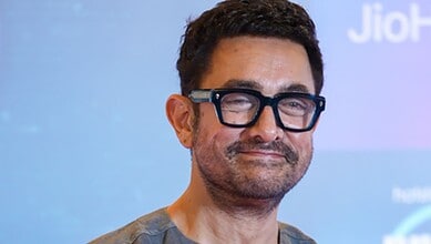 Aamir Khan at a public event, smiling with glasses and a beard.