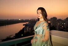 Alia Bhatt standing on balcony during sunset with cityscape in background.