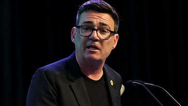 Andy Burnham speaking at a podium during a public event or press conference.