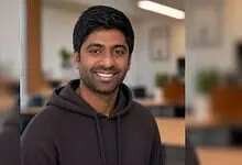 Smiling Indian man in a black hoodie in an office setting.