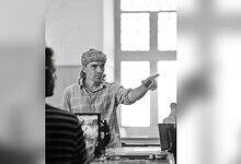 Imtiaz Ali gesturing passionately during a film scene in a bright room.