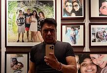 Ram Kapoor taking a selfie in front of a wall of family photos at an exhibition.