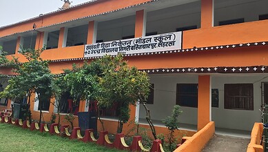 Saffron-coloured school building with a signboard in Hindi and English, surrounded by greenery.