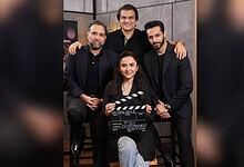 Group of five people, three men and two women, posing with a film clapperboard in a studio setting.