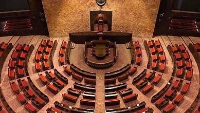 Empty Rajya Sabha chamber with seats and central podium in Parliament House, India.