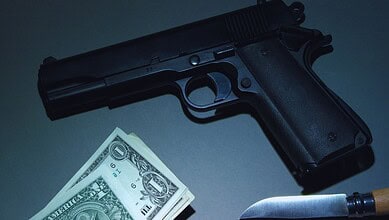 Handgun, cash, and knife arranged on a dark surface, evoking crime or danger.