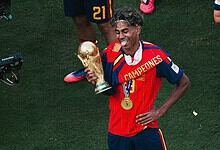 Lamine Yamal celebrating with the World Cup trophy, wearing Spain's red and blue kit.