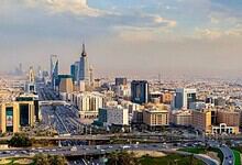 A panoramic view of Riyadh's skyline with modern skyscrapers and highways under a partly cloudy sky.