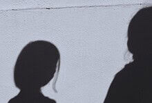 Silhouettes of four school girls against a plain wall, shadowed and indistinct.