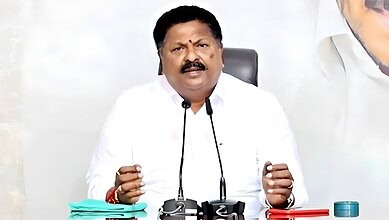 Ex-AP minister speaking at a press conference with microphones and documents on the table.