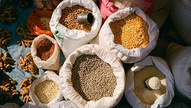 Colorful grains in sacks at a market stall, showcasing diverse types of pulses and cereals.