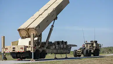 Military missile system being transported by truck on a highway with a support vehicle nearby.