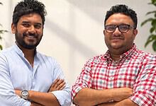 Two smiling men with crossed arms in an office setting, representing startup founders.