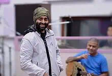 Arijit Singh in a white jacket and turban smiling during a casual event.