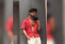 Person in red shirt and white pants taking a mirror selfie, wearing a face mask.