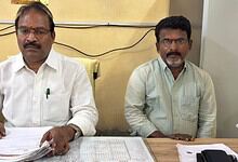 Two men sitting at a desk with documents, in an office setting.