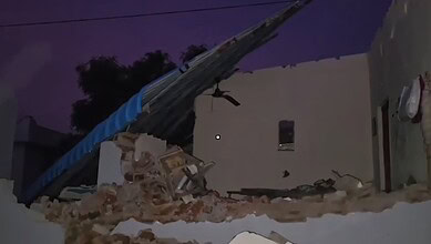 Collapsed building with debris after demolition, dark sky in background.
