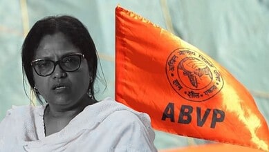 Muslim woman vice-principal speaking at an event with ABVP flag in background.