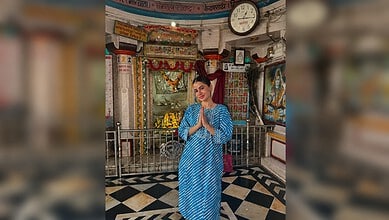 Uorfi Javed in a blue traditional dress praying inside a temple with religious decorations.
